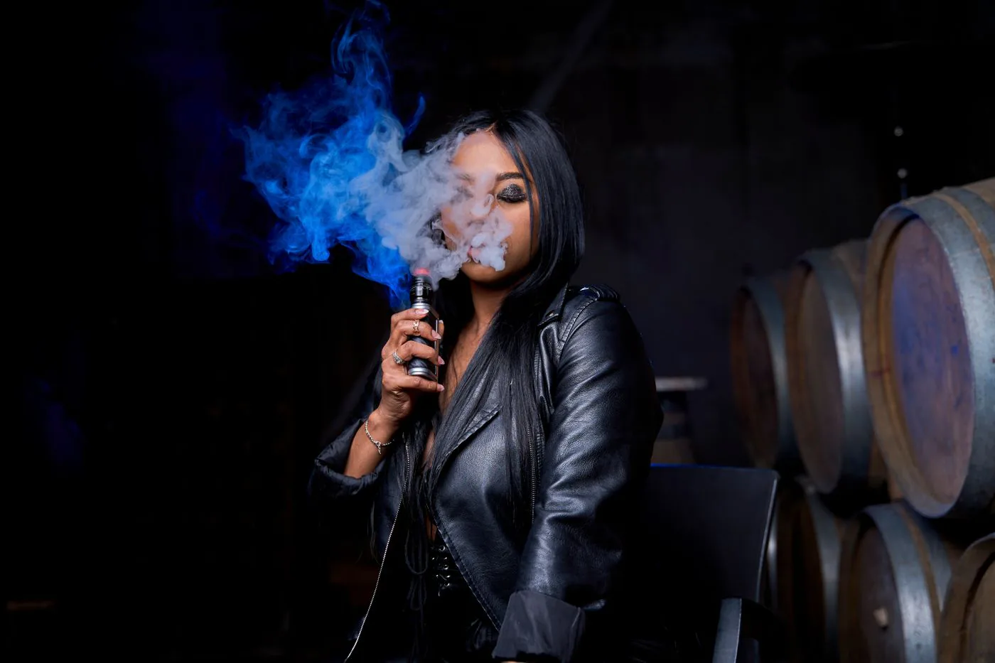 Une femme en veste de cuir expire un nuage de vapeur sous une lumière bleue.