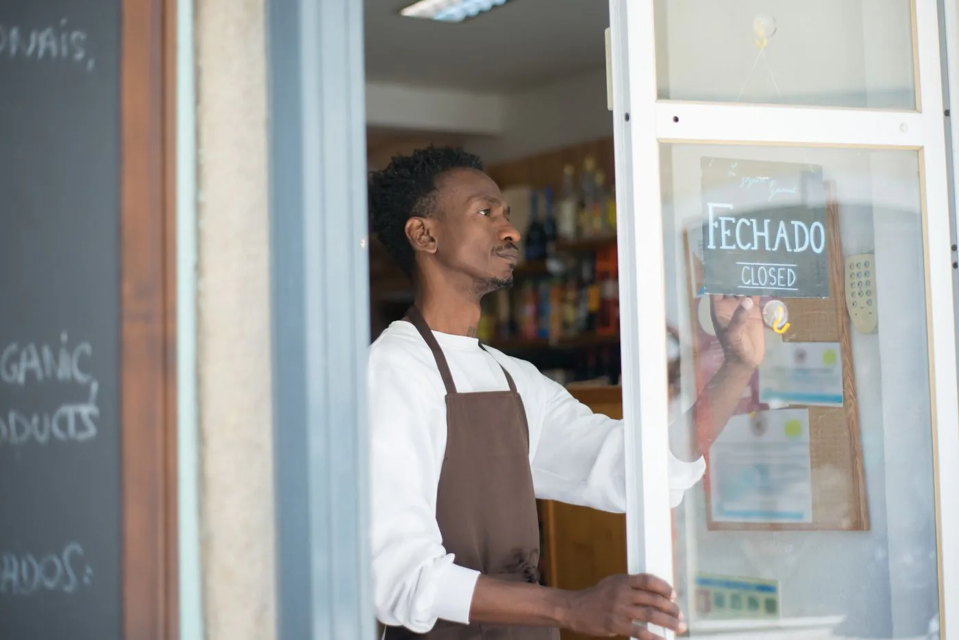 Un commerçant souriant accueille un client à l'entrée de sa boutique.